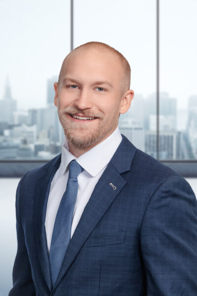 A man in a navy blue suit with a blue tie smiling